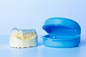 Dental mouth guard on a model of teeth sitting beside a plastic case