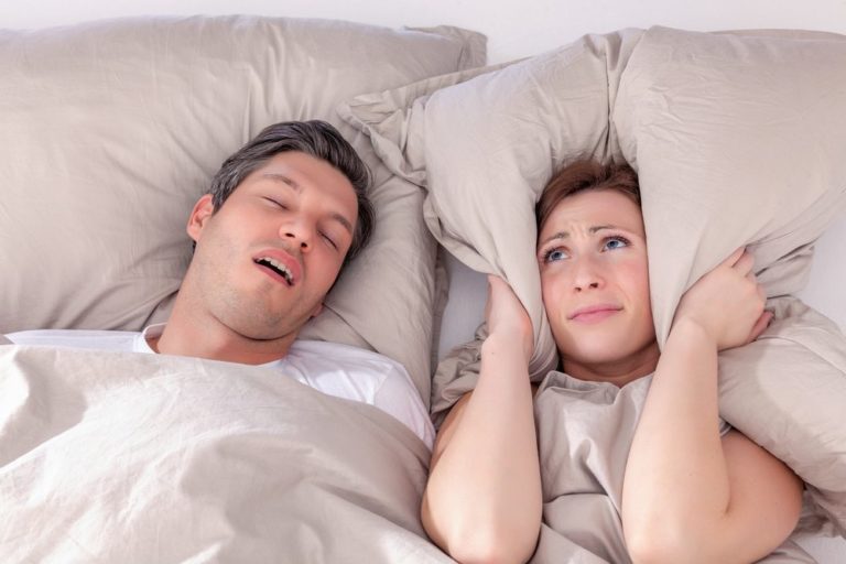 Woman covering her ears with a pillow because of her partners loud snoring from sleep apnea