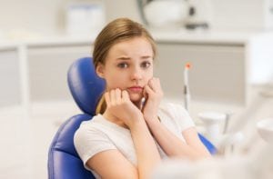A young girl sitting in the dentist chair looking scared