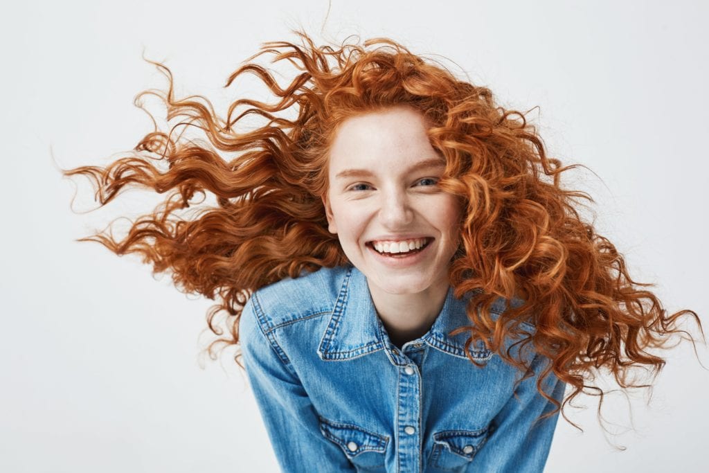 Redhead with curly hair smiling against a white background