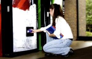 girl with books getting something out of vending machine